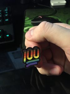 A hand holding up the pride 100 sticker by a finger that it's stuck to.